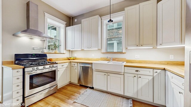 kitchen featuring wood counters, light wood-style flooring, wall chimney exhaust hood, and stainless steel appliances