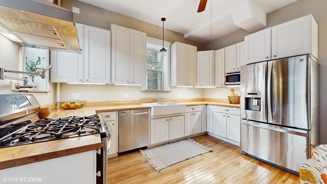kitchen with wall chimney range hood, butcher block countertops, a sink, light wood-type flooring, and stainless steel appliances