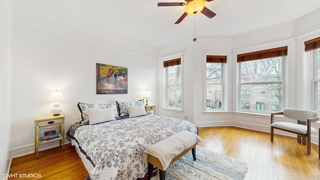 bedroom featuring light wood-style floors, a ceiling fan, baseboards, and multiple windows
