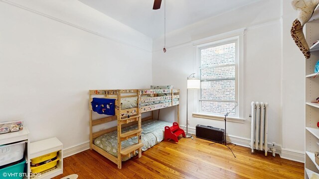 bedroom with radiator, wood finished floors, baseboards, and ceiling fan
