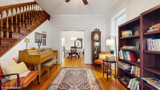 living area with stairway, crown molding, a ceiling fan, and wood finished floors