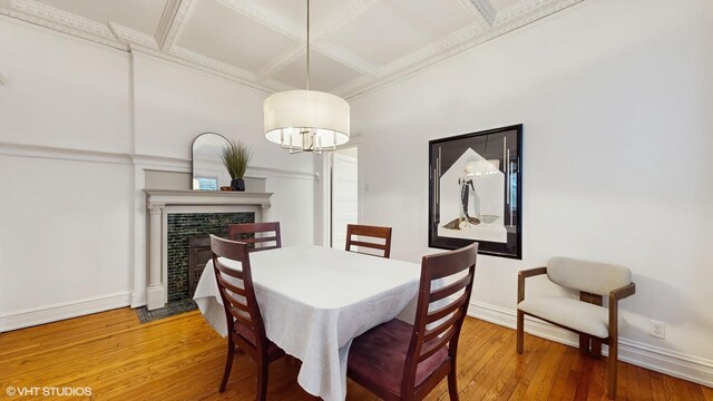 dining space featuring coffered ceiling, light wood-style floors, crown molding, baseboards, and a fireplace