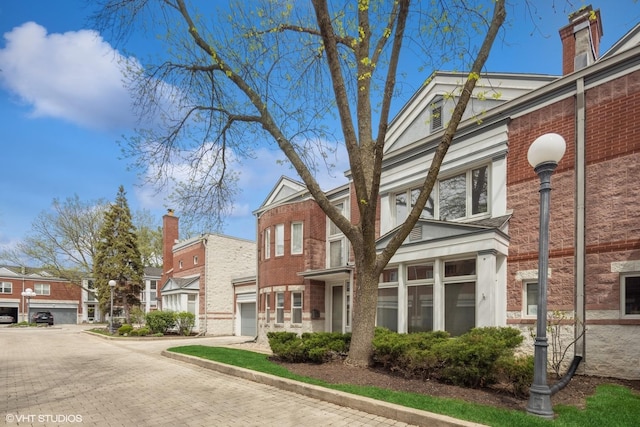 view of side of home with brick siding, a garage, a residential view, and decorative driveway