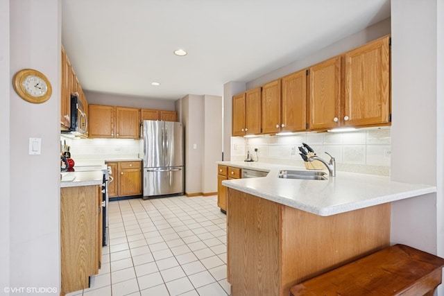 kitchen featuring backsplash, appliances with stainless steel finishes, a sink, light countertops, and a peninsula