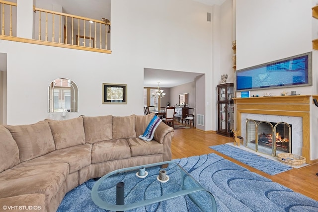 living room with a warm lit fireplace, a towering ceiling, wood finished floors, and a chandelier