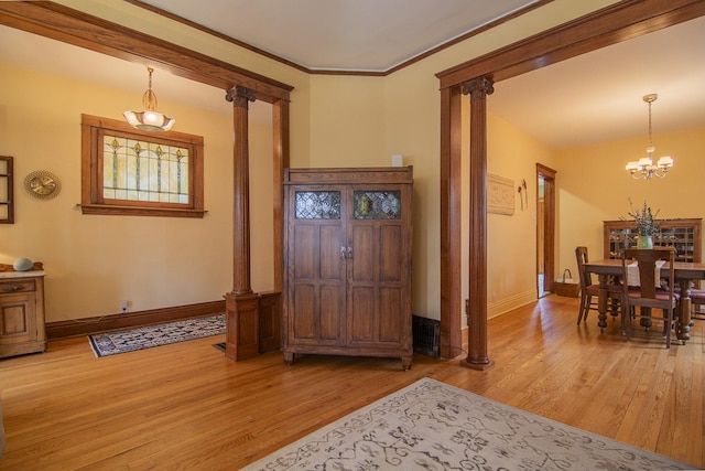 foyer featuring baseboards, a notable chandelier, light wood finished floors, and decorative columns