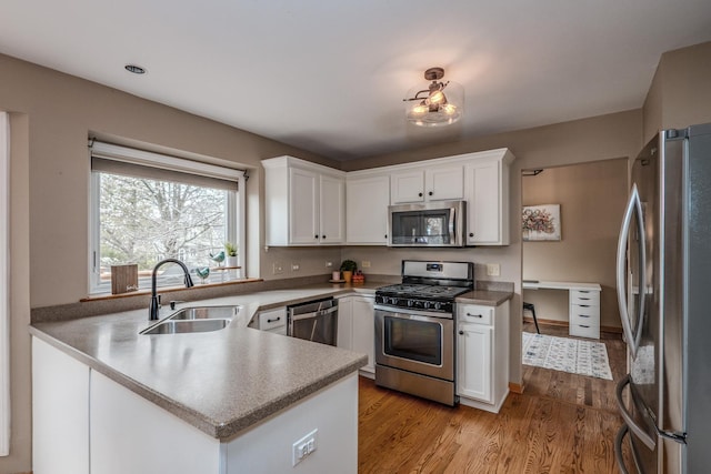 kitchen featuring a peninsula, white cabinetry, stainless steel appliances, and a sink