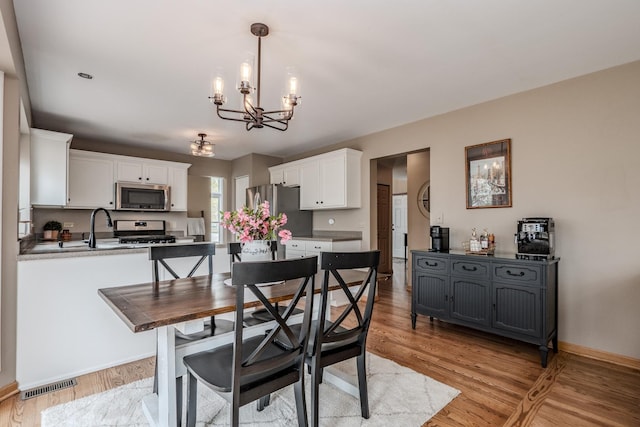 dining space featuring light wood-type flooring, visible vents, baseboards, and an inviting chandelier