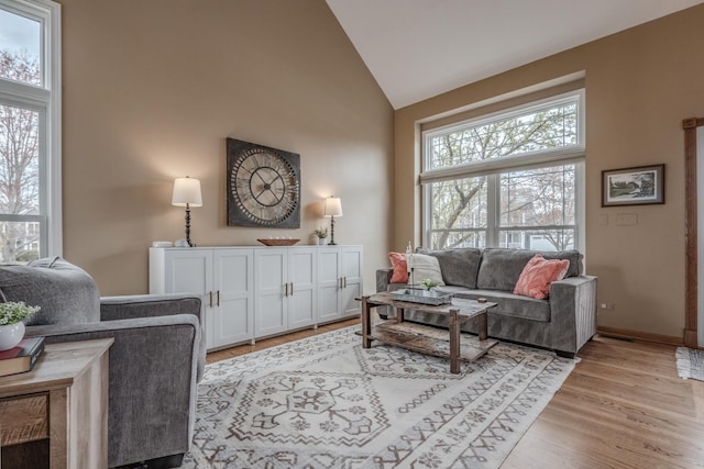 living room with light wood-type flooring, baseboards, and high vaulted ceiling