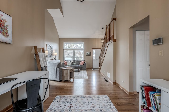 foyer with baseboards, wood finished floors, high vaulted ceiling, and stairway