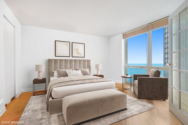 bedroom featuring baseboards, wood finished floors, a water view, and multiple windows