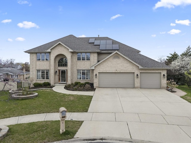 traditional-style house with solar panels, driveway, an attached garage, a shingled roof, and a front yard
