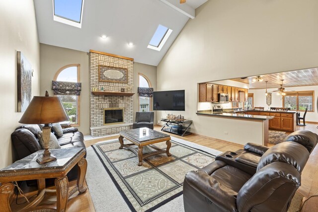 living room featuring light wood-style floors, high vaulted ceiling, a skylight, beamed ceiling, and a fireplace