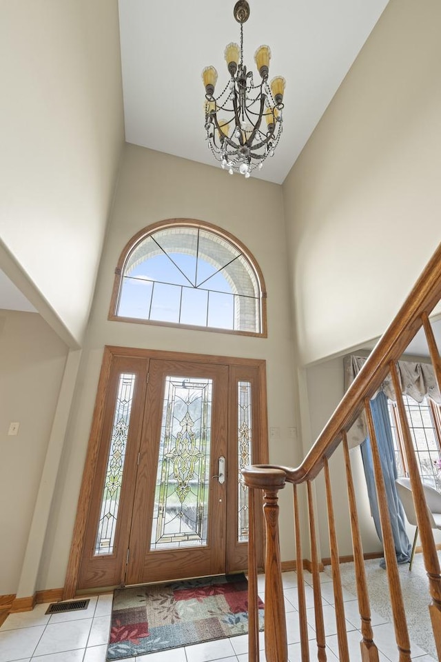 entryway featuring stairway, light tile patterned floors, an inviting chandelier, a towering ceiling, and visible vents