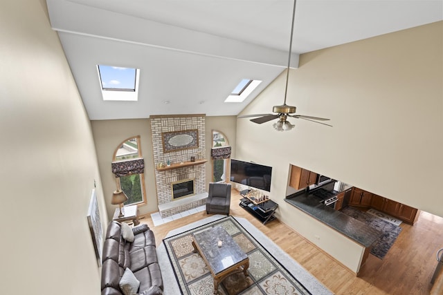 living room with high vaulted ceiling, a skylight, wood finished floors, ceiling fan, and a fireplace