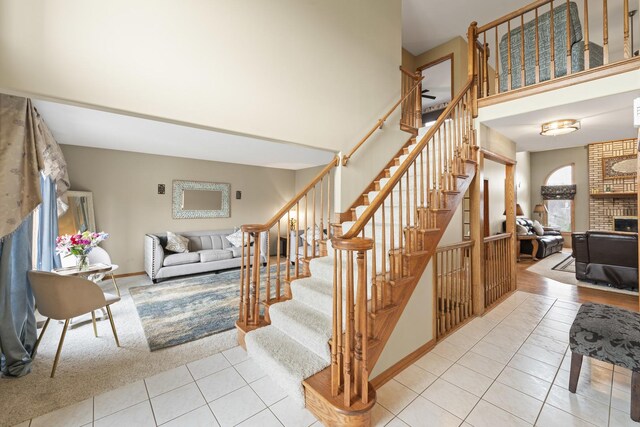 staircase with carpet floors, baseboards, a towering ceiling, tile patterned flooring, and a fireplace
