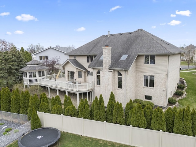 back of property featuring a chimney, a shingled roof, a fenced backyard, brick siding, and a gazebo