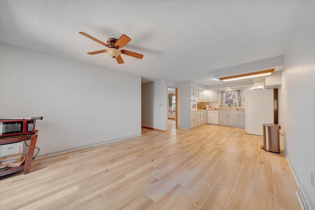 unfurnished living room featuring baseboards, a ceiling fan, a textured ceiling, and light wood-style flooring