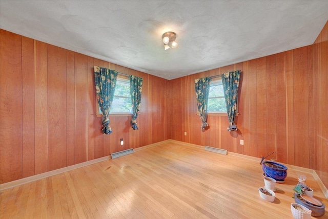 unfurnished room with wood walls, visible vents, a wealth of natural light, and wood finished floors