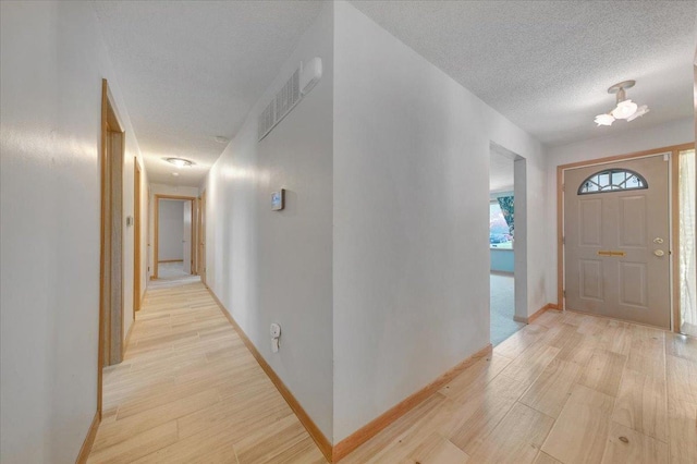 foyer entrance featuring visible vents, a textured ceiling, light wood finished floors, and baseboards
