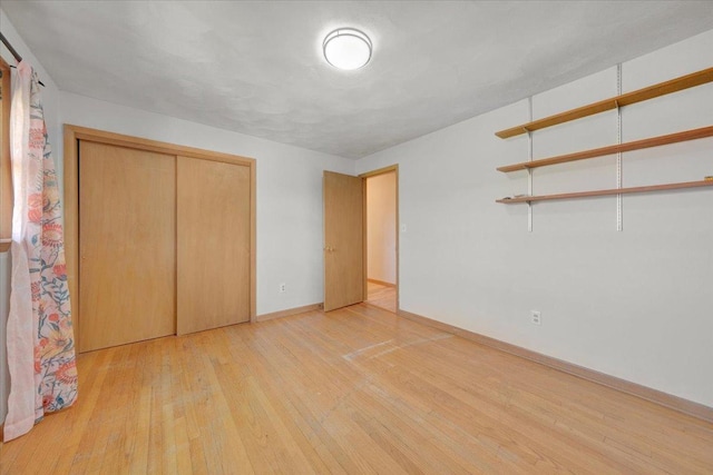 unfurnished bedroom with a closet, baseboards, and light wood-type flooring