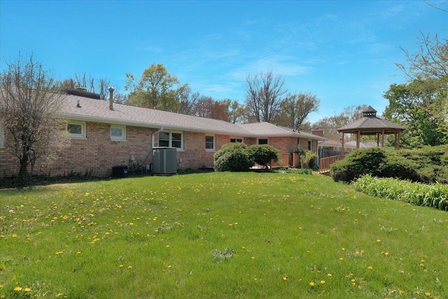 rear view of property featuring a gazebo, brick siding, central AC unit, a chimney, and a yard
