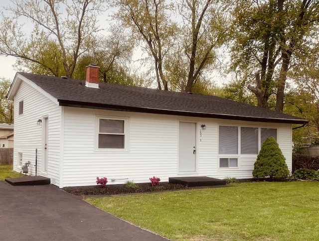 single story home featuring a shingled roof, a chimney, and a front yard