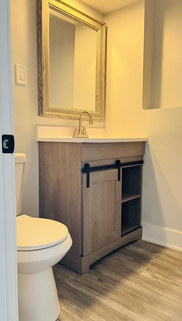 half bathroom featuring vanity, baseboards, toilet, and wood finished floors