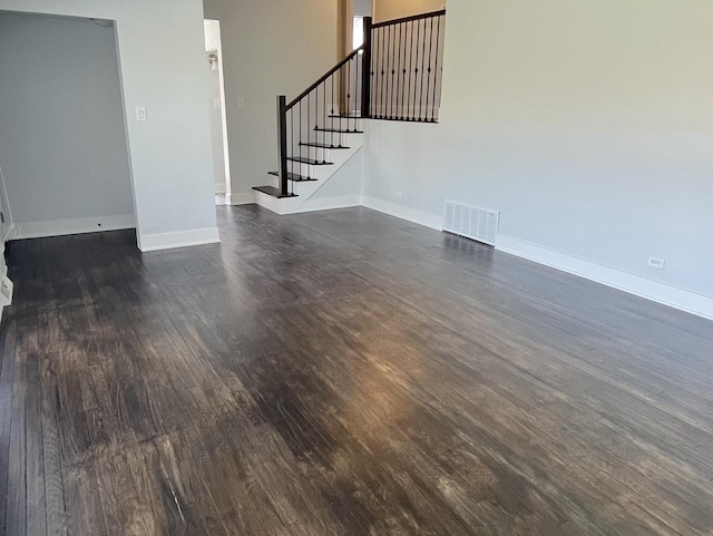 unfurnished living room featuring baseboards, visible vents, dark wood-style floors, and stairway