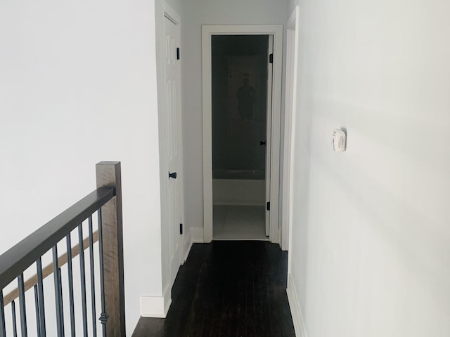 corridor with baseboards, an upstairs landing, and wood finished floors
