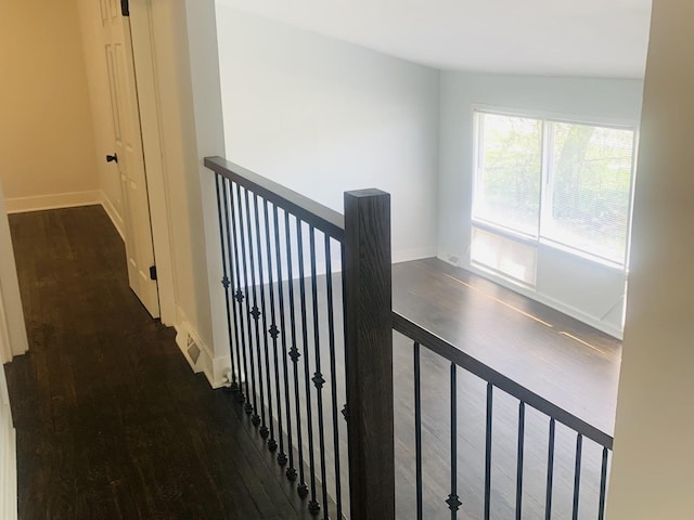 hallway featuring baseboards, wood finished floors, and an upstairs landing