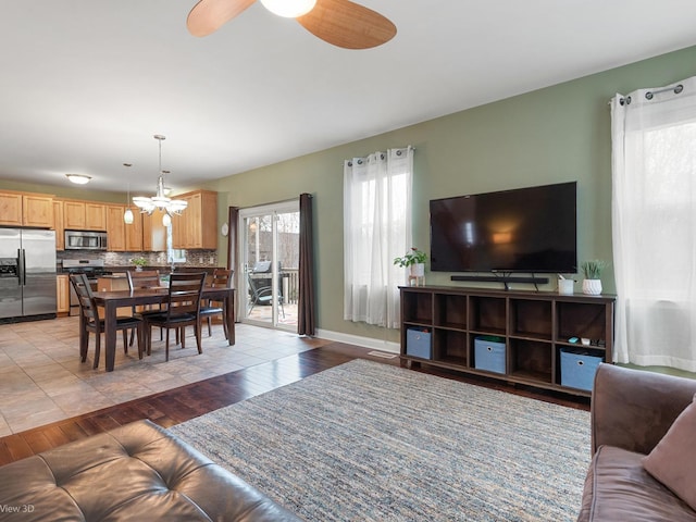 living area featuring baseboards, light wood-style flooring, and ceiling fan with notable chandelier