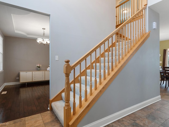 stairs featuring baseboards, an inviting chandelier, and a raised ceiling