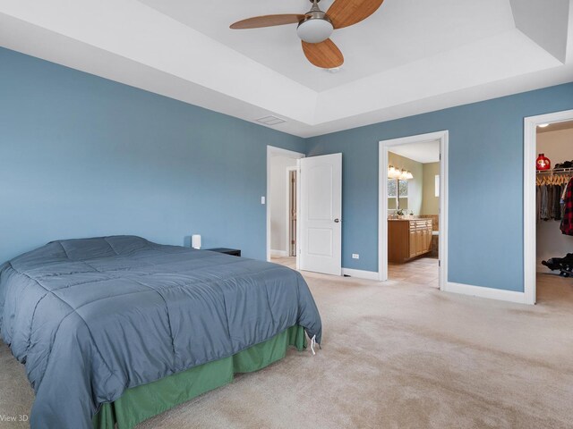 bedroom featuring a closet, light carpet, baseboards, a walk in closet, and a raised ceiling