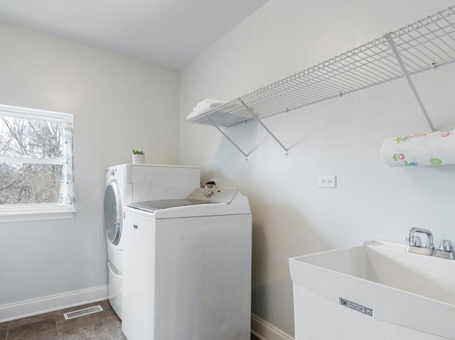 washroom with laundry area, visible vents, washer and dryer, baseboards, and a sink
