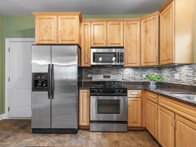 kitchen with light brown cabinetry, stone finish floor, dark stone counters, stainless steel appliances, and tasteful backsplash