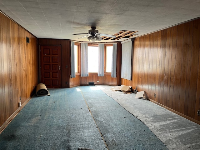 carpeted empty room featuring baseboards, wood walls, and ceiling fan