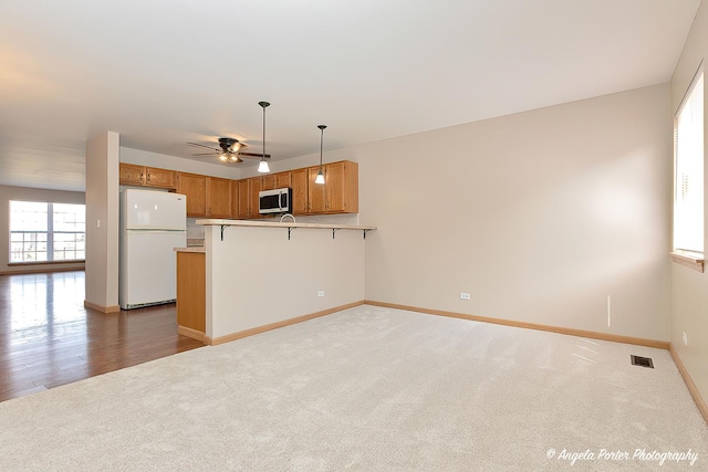 kitchen featuring a peninsula, stainless steel microwave, freestanding refrigerator, light colored carpet, and ceiling fan