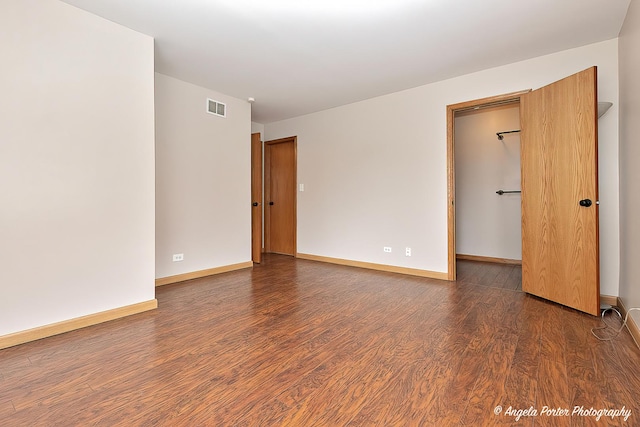 unfurnished bedroom with a walk in closet, baseboards, wood finished floors, and visible vents