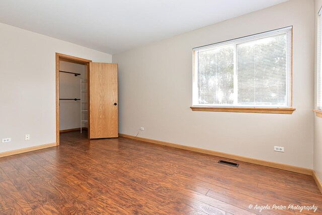 unfurnished bedroom with wood finished floors, a spacious closet, baseboards, and visible vents