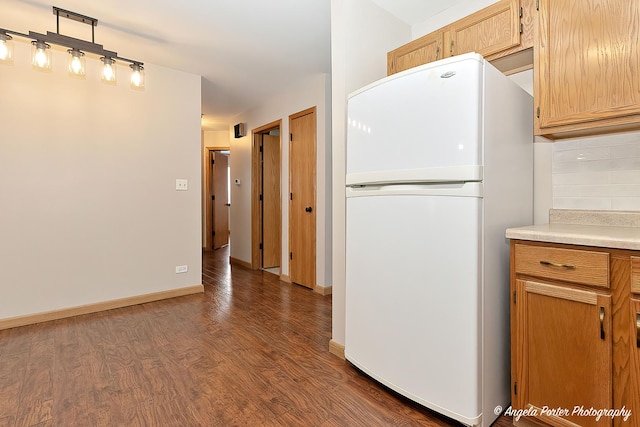 kitchen with backsplash, light countertops, dark wood-type flooring, freestanding refrigerator, and baseboards