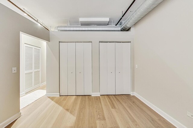 unfurnished bedroom featuring wood finished floors, multiple closets, and baseboards