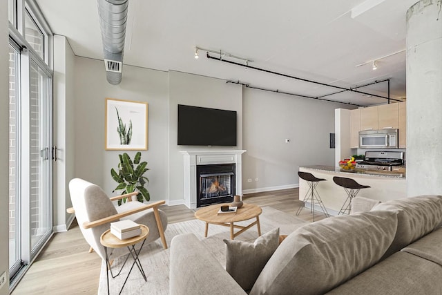 living room with rail lighting, baseboards, a glass covered fireplace, and light wood-style flooring