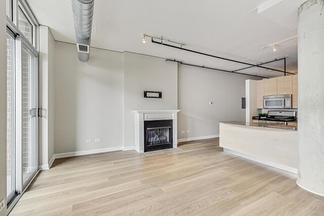 unfurnished living room featuring a fireplace with flush hearth, baseboards, and light wood finished floors