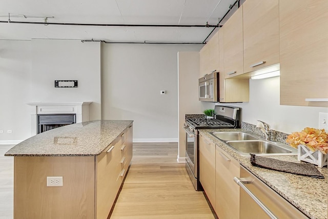 kitchen featuring a center island, a sink, light wood-style floors, light brown cabinets, and appliances with stainless steel finishes