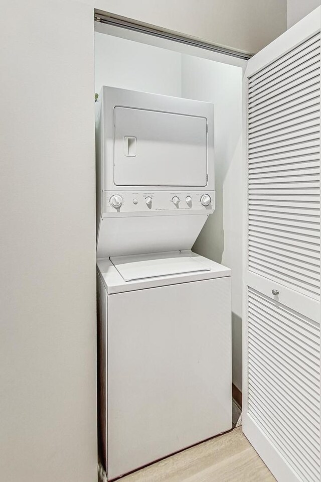 clothes washing area with stacked washer and dryer, laundry area, and light wood-type flooring