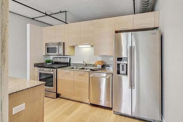kitchen featuring light brown cabinetry, a sink, light wood-style floors, light stone counters, and appliances with stainless steel finishes