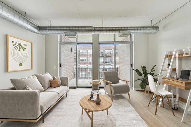 living room with expansive windows, light wood-style floors, and baseboards
