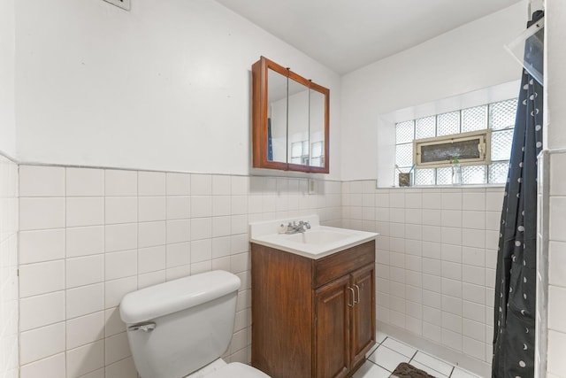 bathroom with tile patterned floors, toilet, tile walls, wainscoting, and vanity