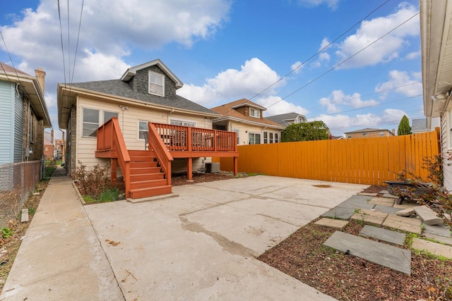 back of property featuring a wooden deck, a patio area, a shingled roof, and a fenced backyard